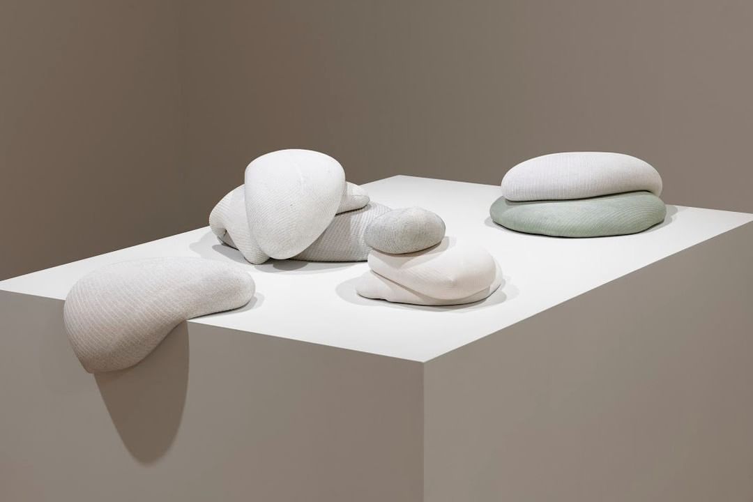 Nine white organic forms stacked in three piles on a white pedestal, one hangs partially over the edge.